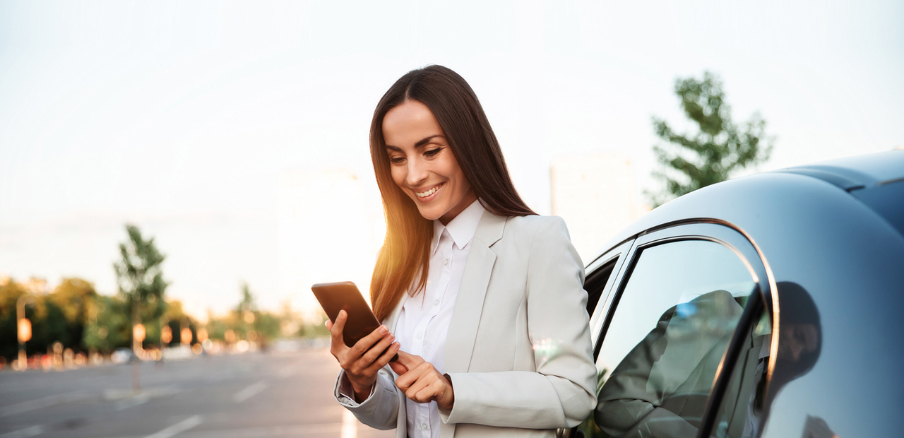 Woman standing next to her car looking at her smartphone